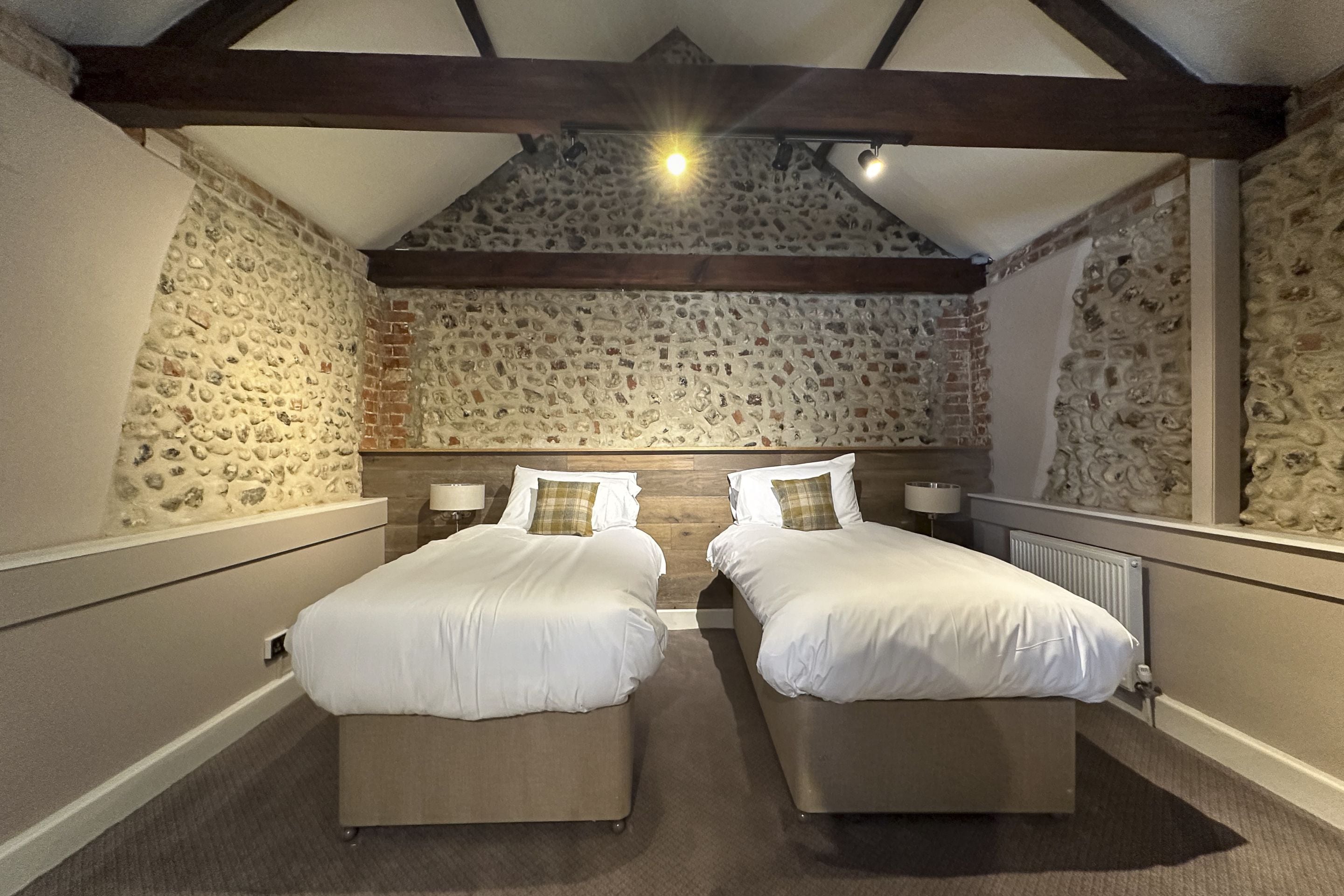 A room with two beds, a stone wall, wooden beams, and a ceiling light.