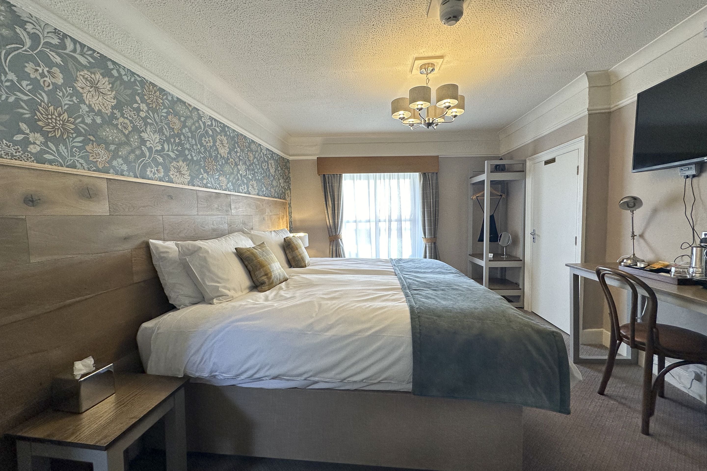A hotel room with a double bed, a desk, a chair, a television, and a wardrobe.