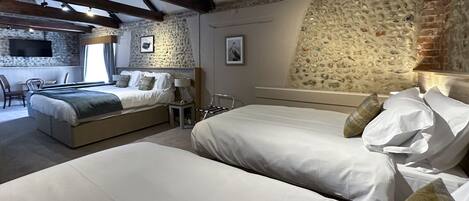 Un dormitorio con dos camas, una pared de piedra y un televisor.