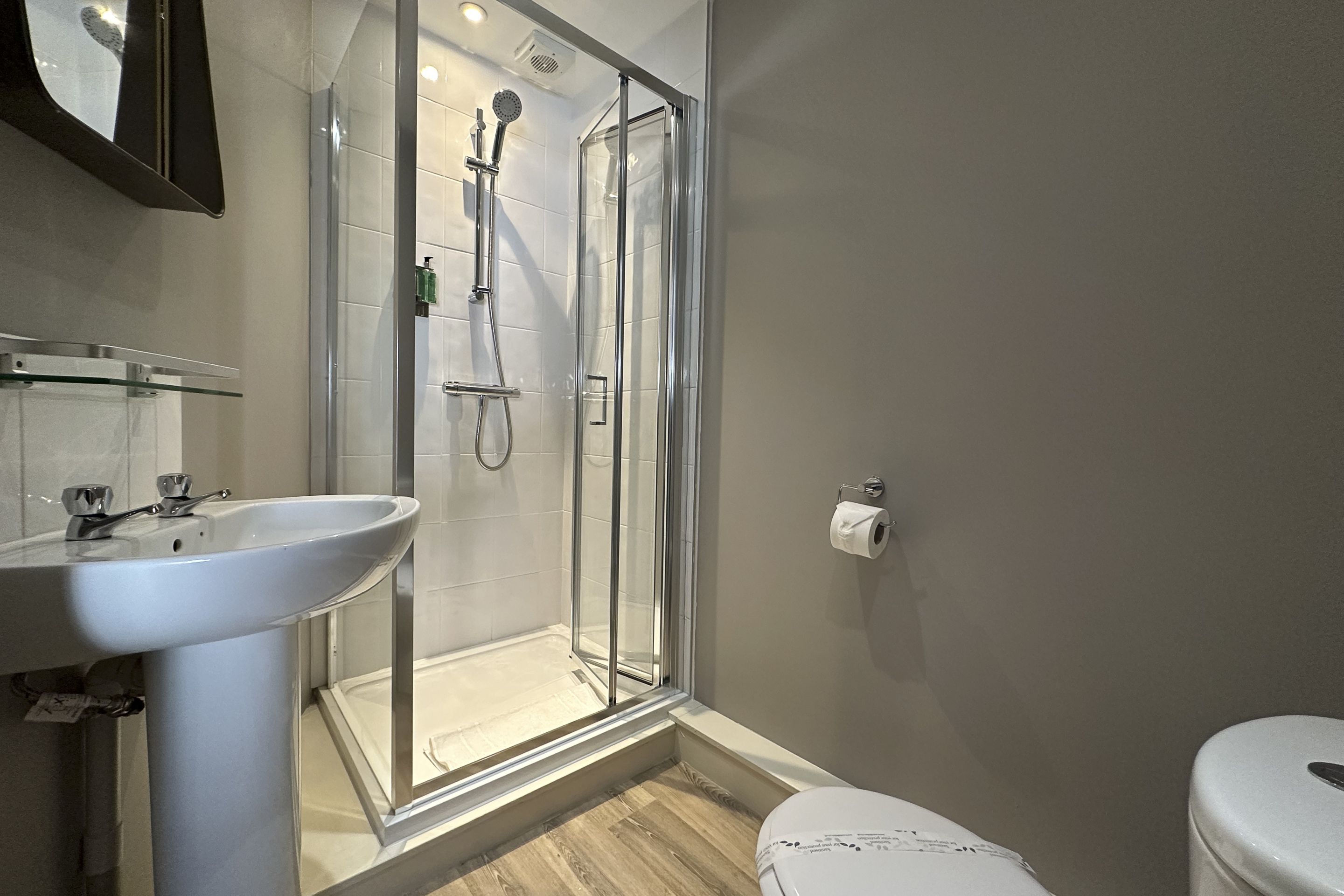 Un baño con ducha cubierta por vidrio, lavamanos blanco y un inodoro.