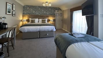 A hotel room with a bed, bedside tables, a desk, and a chair. There is a window with curtains.