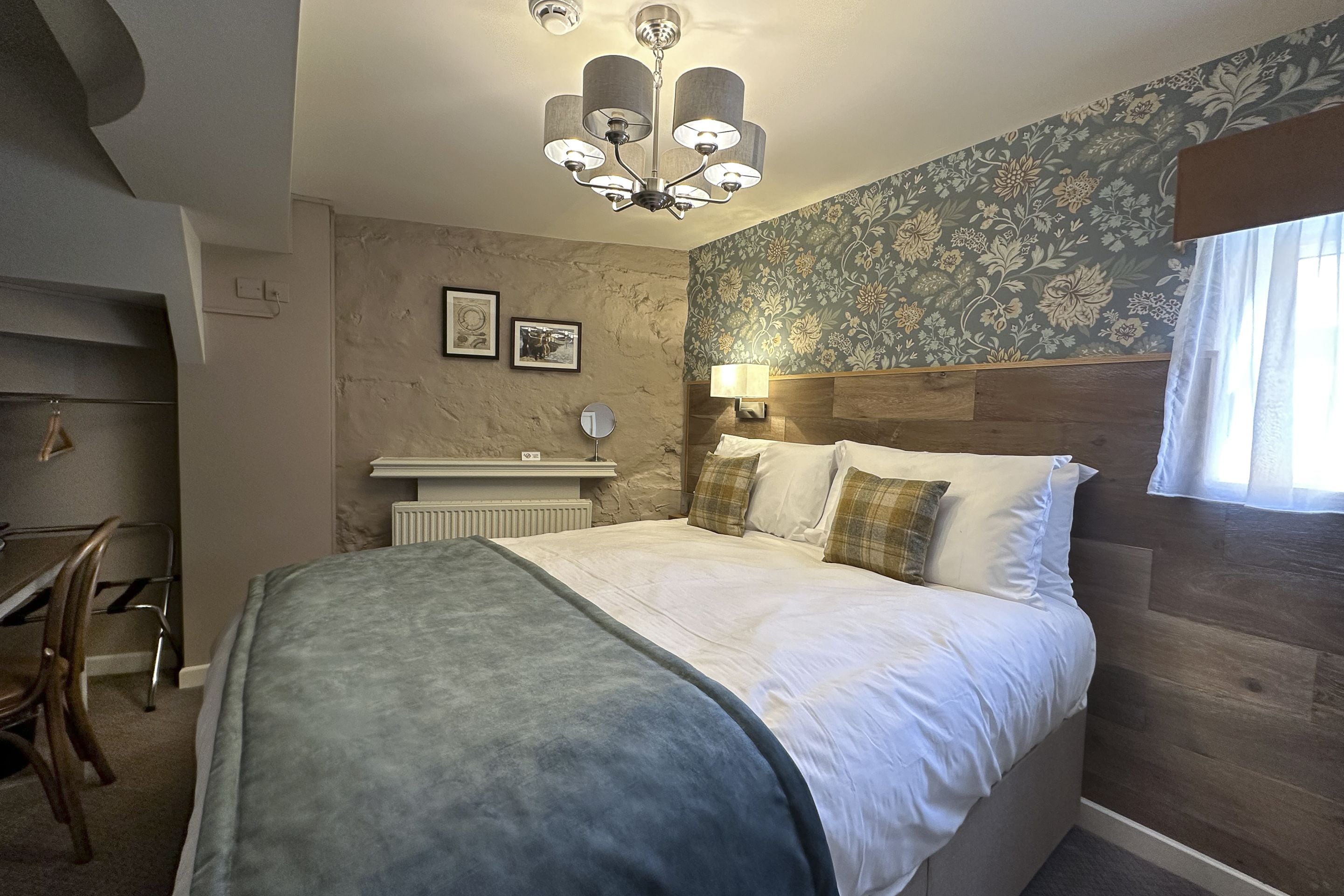 A bedroom with a bed, a nightstand, a mirror, a wall-mounted lamp, and a window with curtains.