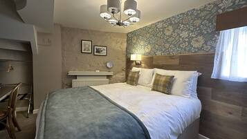 A bedroom with a bed, a nightstand, a mirror, a wall-mounted lamp, and a window with curtains.
