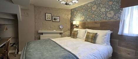 A bedroom with a bed, a nightstand, a mirror, a wall-mounted lamp, and a window with curtains.