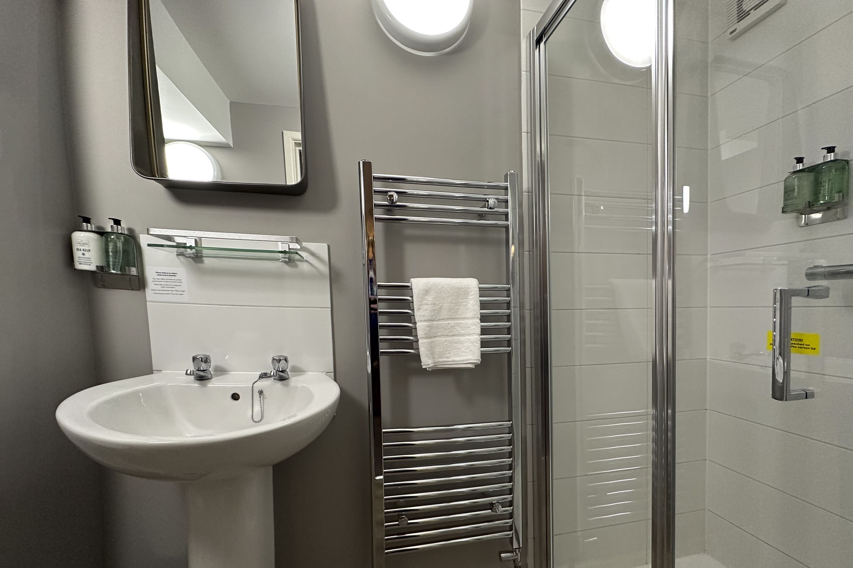 A bathroom with a white sink, a mirror, a glass shower enclosure, and a towel rack.