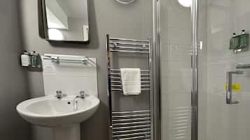A bathroom with a white sink, a mirror, a glass shower enclosure, and a towel rack.