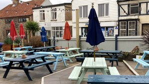 An outdoor seating area with picnic tables and umbrellas, a building with a sign 'Sheringham Shed', and a 'Holiday Inn Express' sign in the background. - The Lobster  (Sheringham)