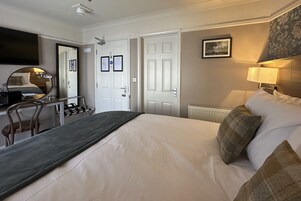 Una habitación de hotel con cama, escritorio, silla, espejo y radiador.