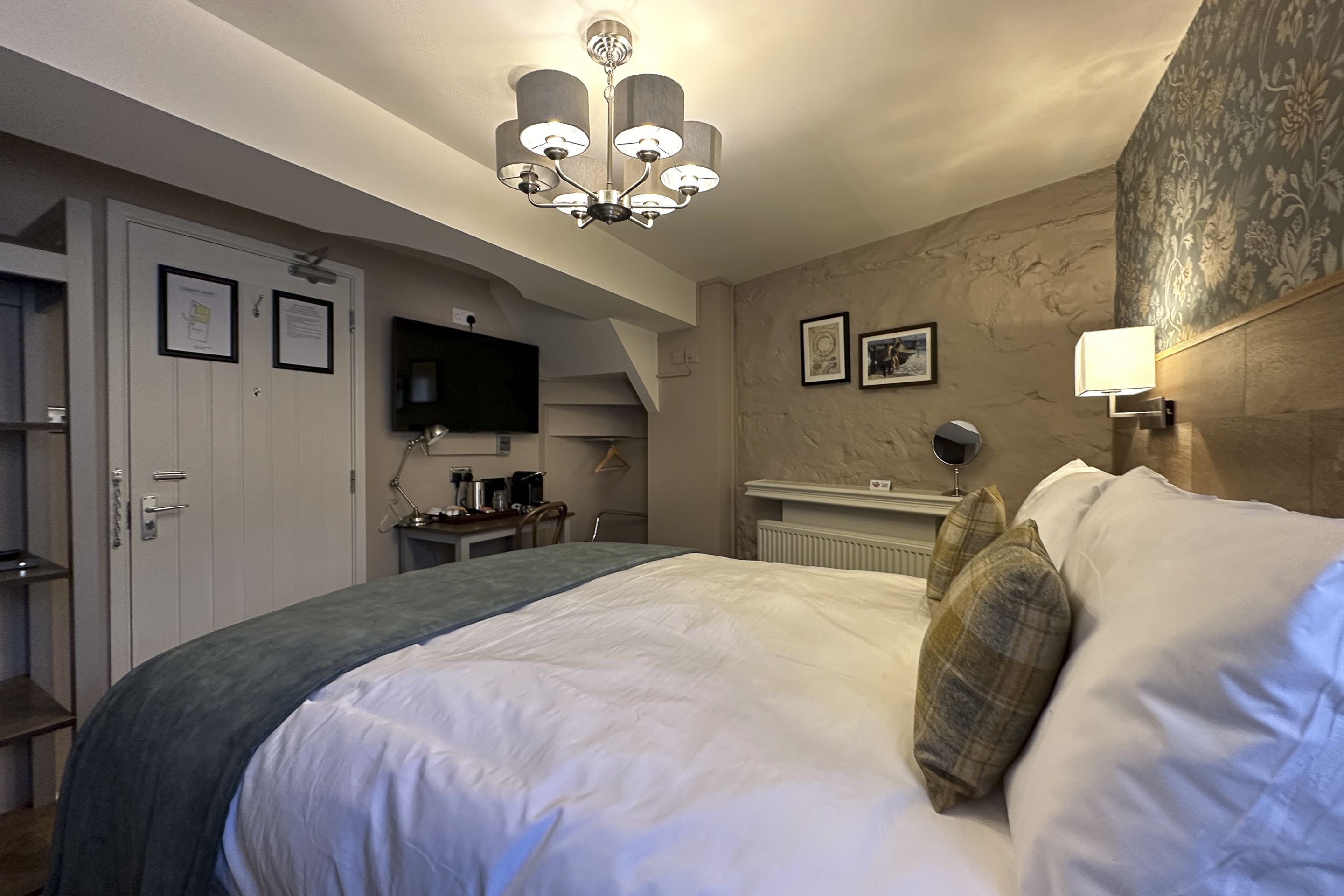 Una habitación de hotel con una cama grande, un televisor, un escritorio con cafetera y una araña.