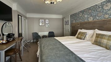Una habitación de hotel con una cama, un escritorio con una silla, un televisor y un espejo.