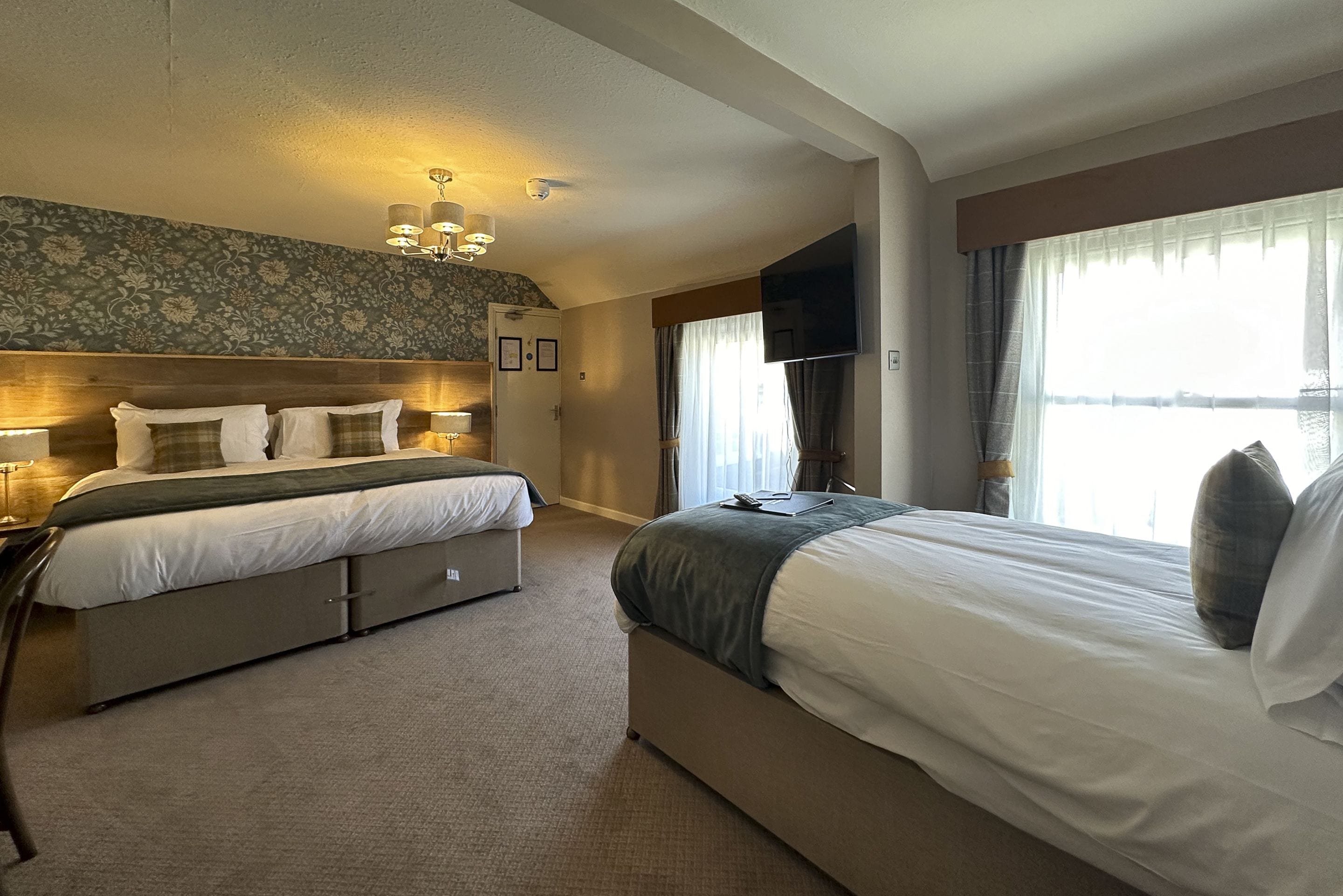 A hotel room with a large bed, a smaller bed, a desk, a TV, and a view of the outdoors.