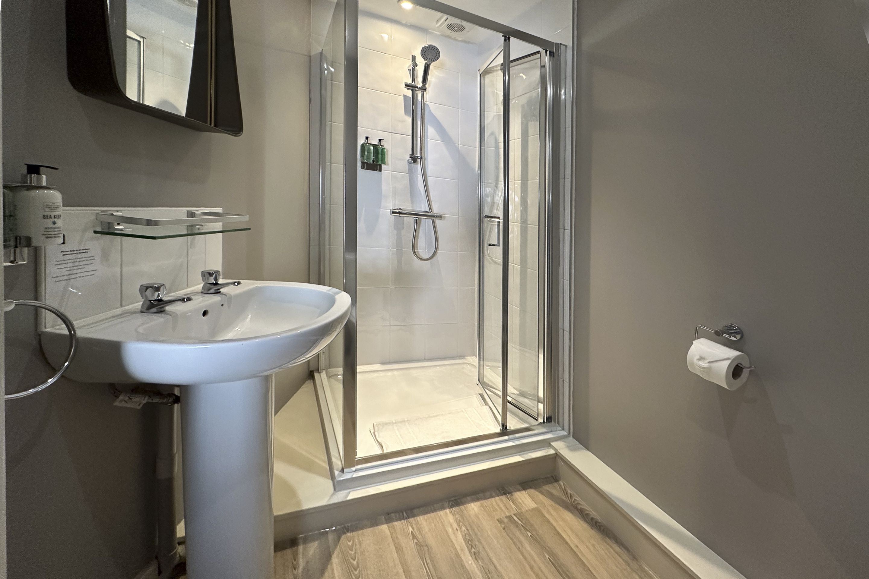 A modern bathroom with a glass shower enclosure, a pedestal sink, and a toilet paper holder.
