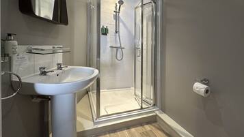 A modern bathroom with a glass shower enclosure, a pedestal sink, and a toilet paper holder.