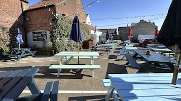 An outdoor seating area with picnic tables and umbrellas, a brick building, and string lights.
