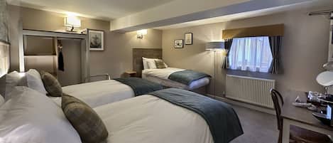 A hotel room with two beds, a desk, a chair, a radiator, and a window with curtains.
