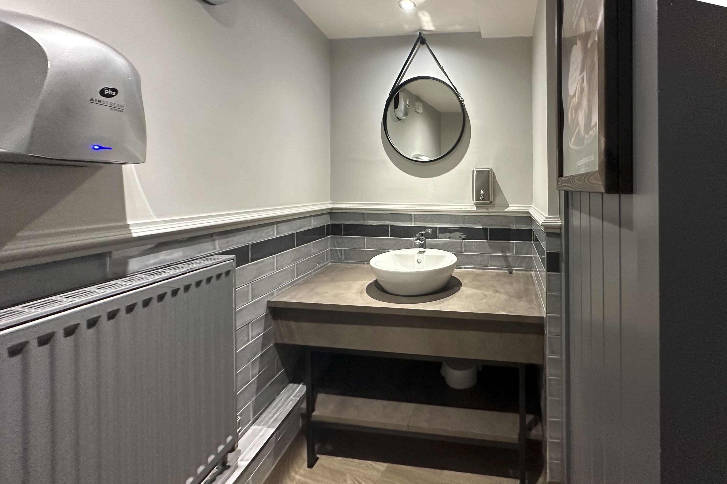 A bathroom with a white sink, a mirror, a hand dryer, and a radiator.