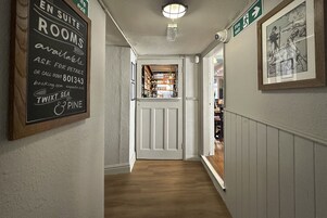 Un pasillo con un letrero que indica disponibilidad de suites, un área de bar visible a través de una puerta y un cuadro en la pared.