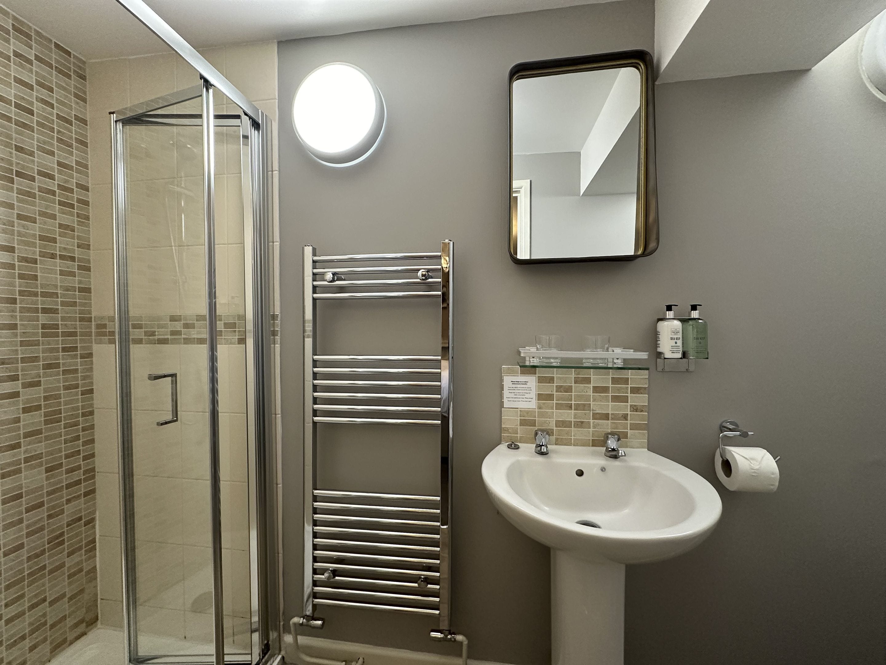 A bathroom with a glass shower enclosure, a chrome towel rack, a white sink, and a mirror.