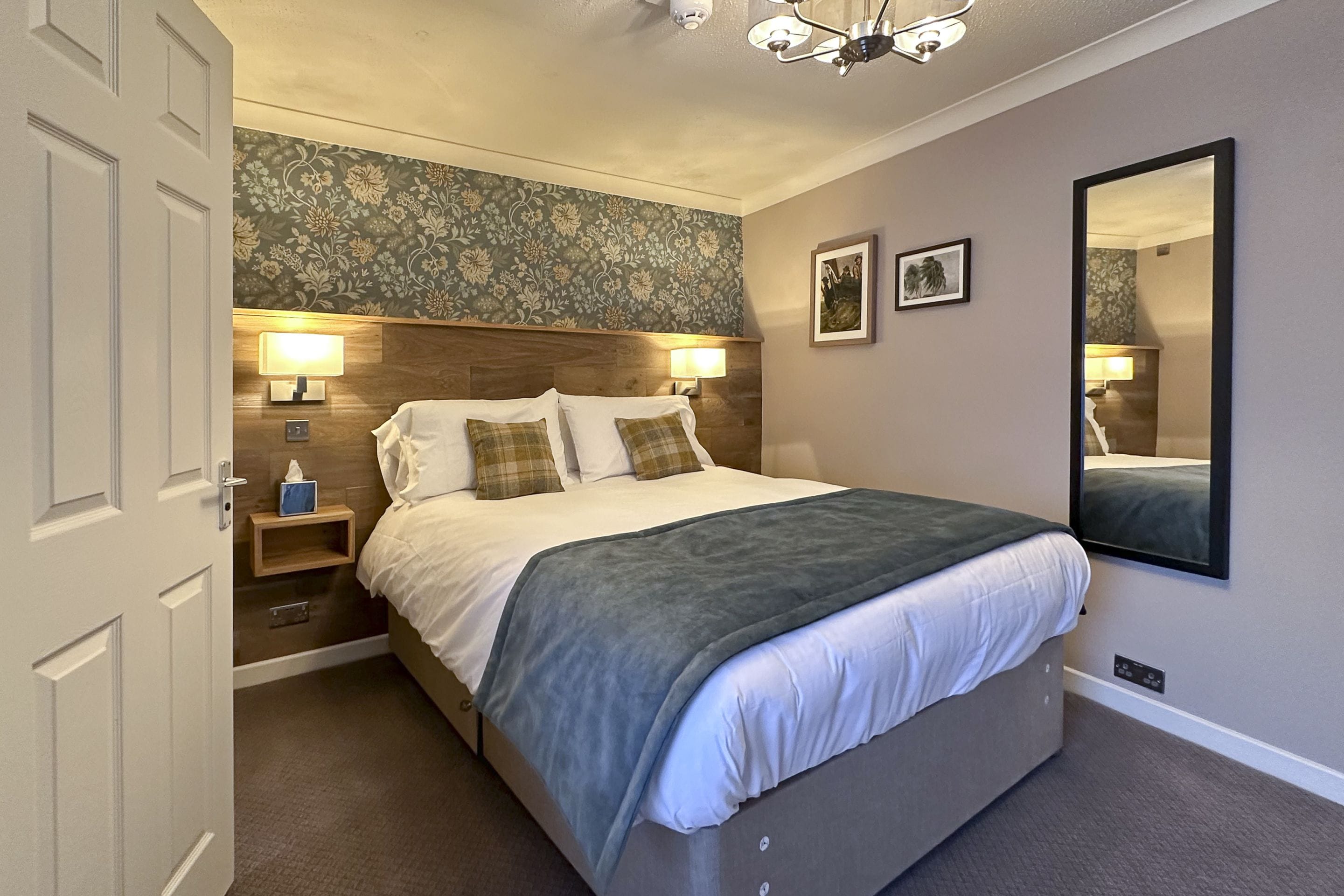 A bedroom with a bed, bedside lamps, a nightstand, a mirror, and a door.