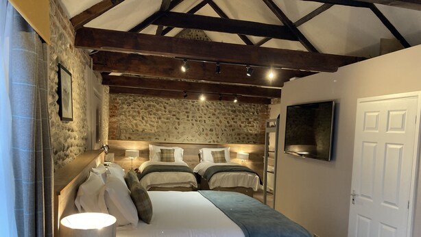 A bedroom with a stone wall, wooden beams, a TV, and a bed with a bedside table. - The Lobster  (Sheringham)