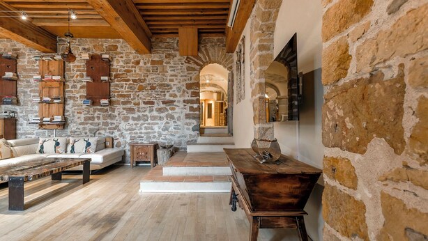 A rustic interior with exposed stone walls, wooden beams, a sofa, a wooden table, and a staircase leading to an upper level. - Appartement de Standing au Cœur du Vieux Lyon (Lyon)