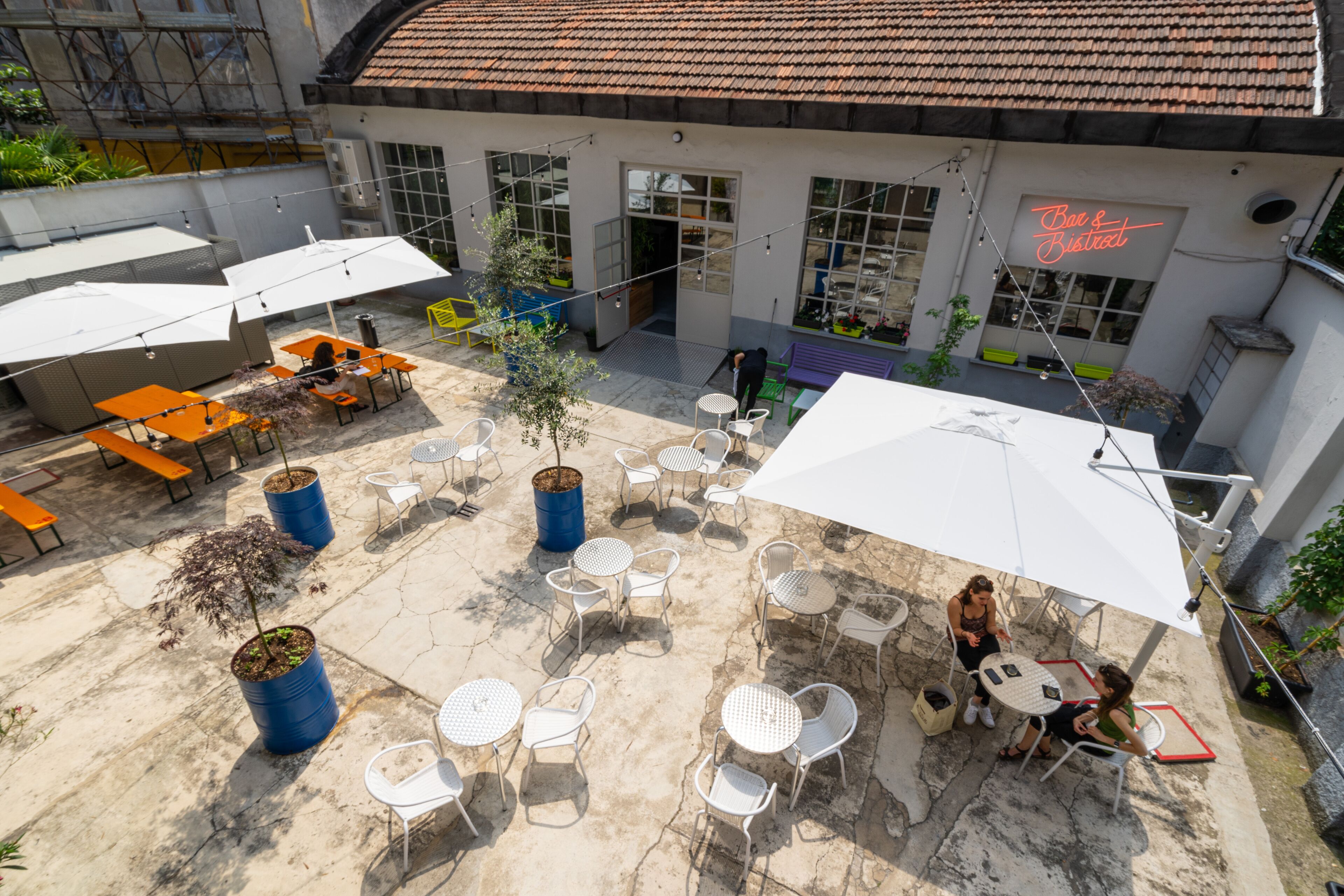 An outdoor patio area with tables and chairs, potted plants, and umbrellas.