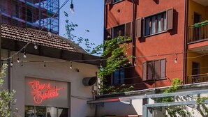 Un café al aire libre con mesas y sillas, un letrero de neón y un edificio con balcones.