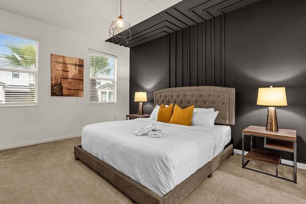A bedroom with a large bed, two bedside lamps, a wooden nightstand, and a window with blinds.