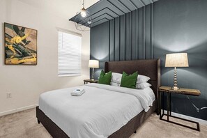 Quarto com cama, duas mesas de cabeceira com luminárias, uma janela com persianas e um quadro na parede.