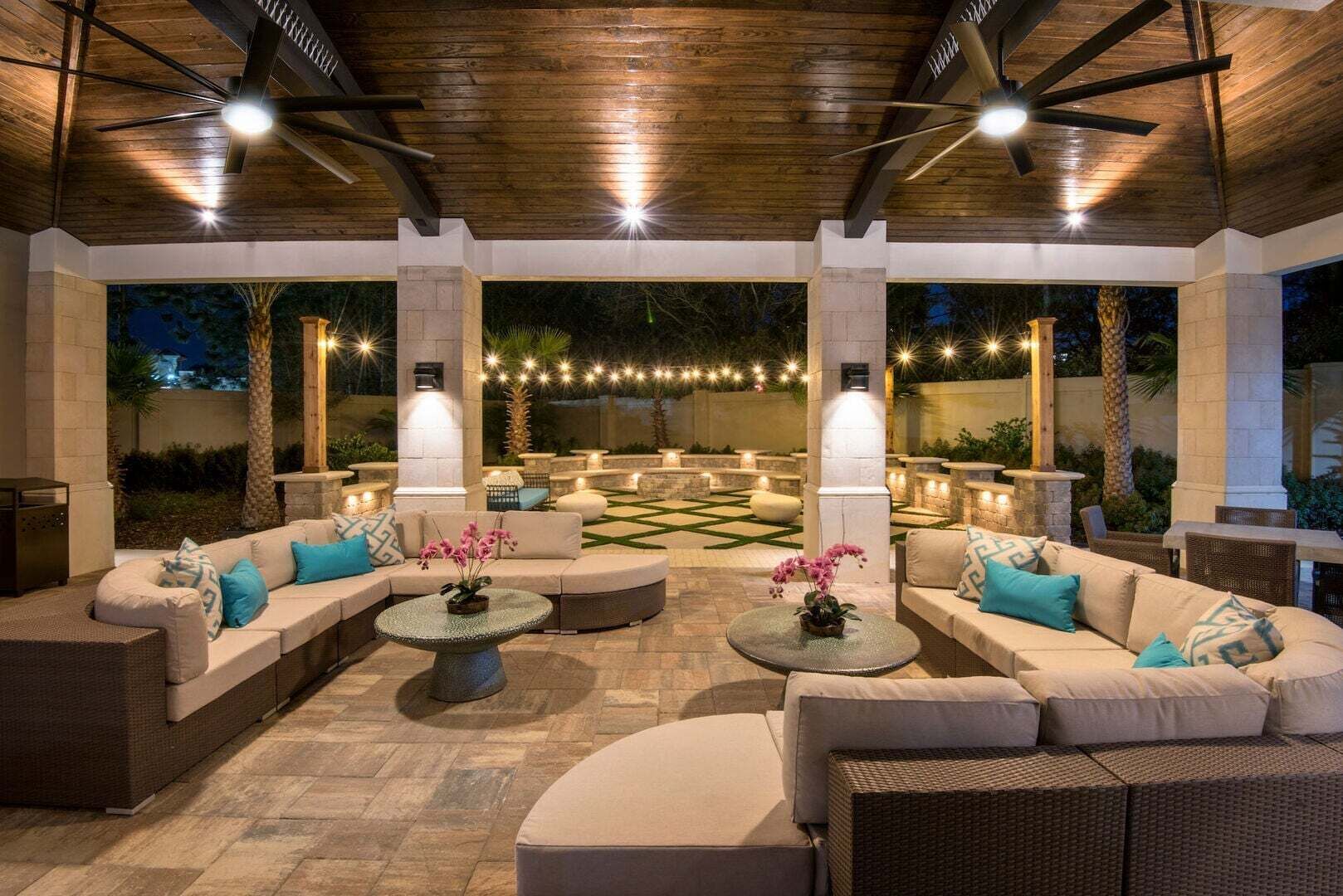 An outdoor patio with a wooden ceiling, multiple seating areas, and string lights.