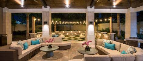An outdoor patio with a wooden ceiling, multiple seating areas, and string lights.