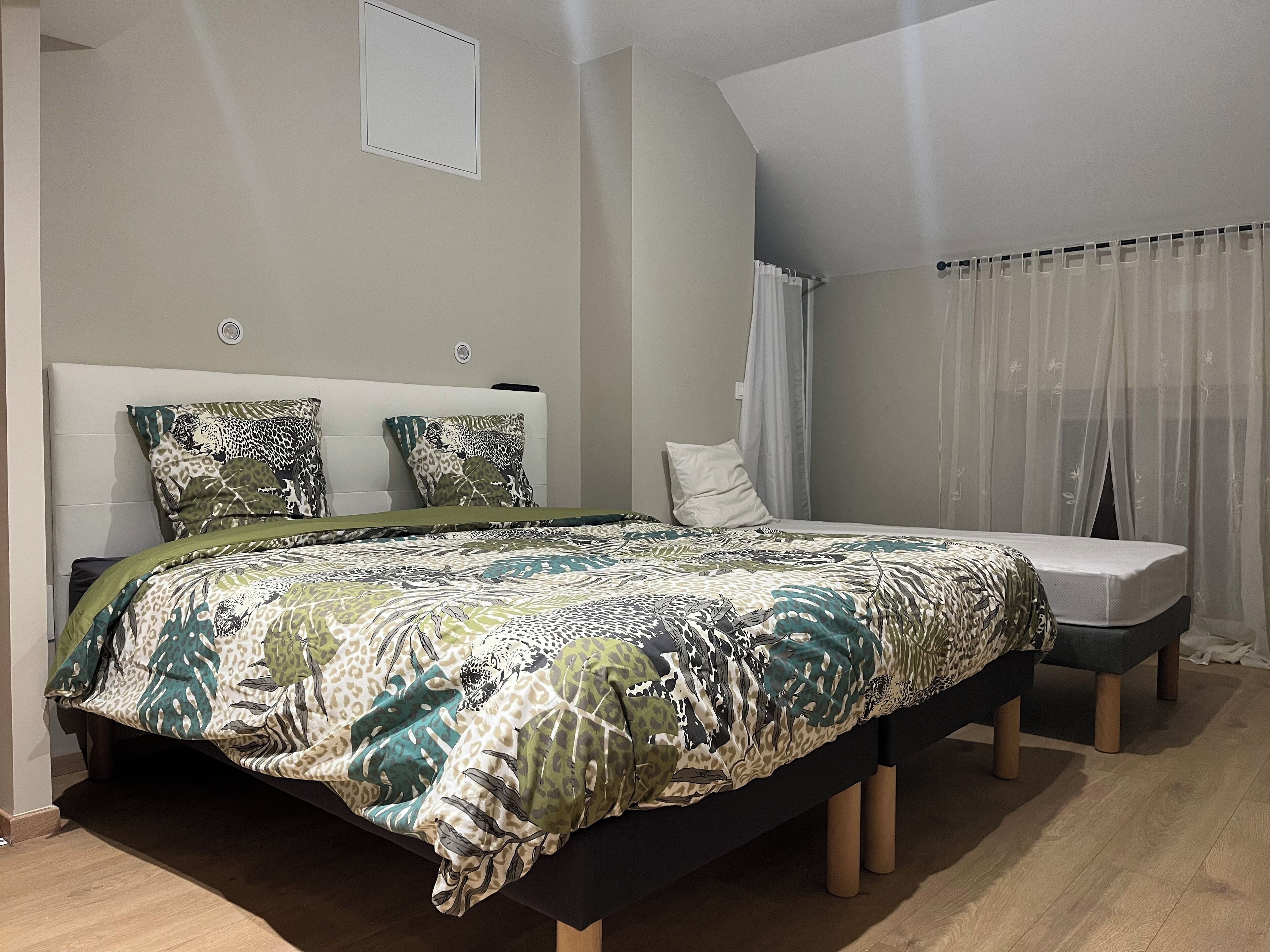 Un dormitorio con cama, cabecera, mesita de noche y ventana con cortinas.