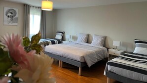 A hotel room with two beds, a bedside table with a lamp, a ceiling light, and a window with curtains.