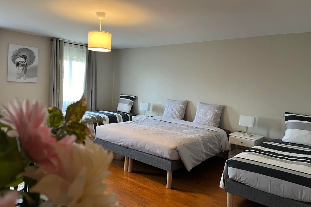 A hotel room with two beds, a bedside table with a lamp, a ceiling light, and a window with curtains.