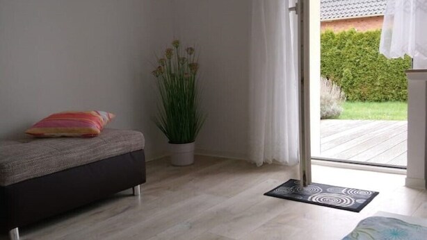 A room with a sofa, a potted plant, a door leading outside, and a mat on the floor. - Gästehaus Barbara mit Garage in 26919 Brake (Brake (Unterweser))