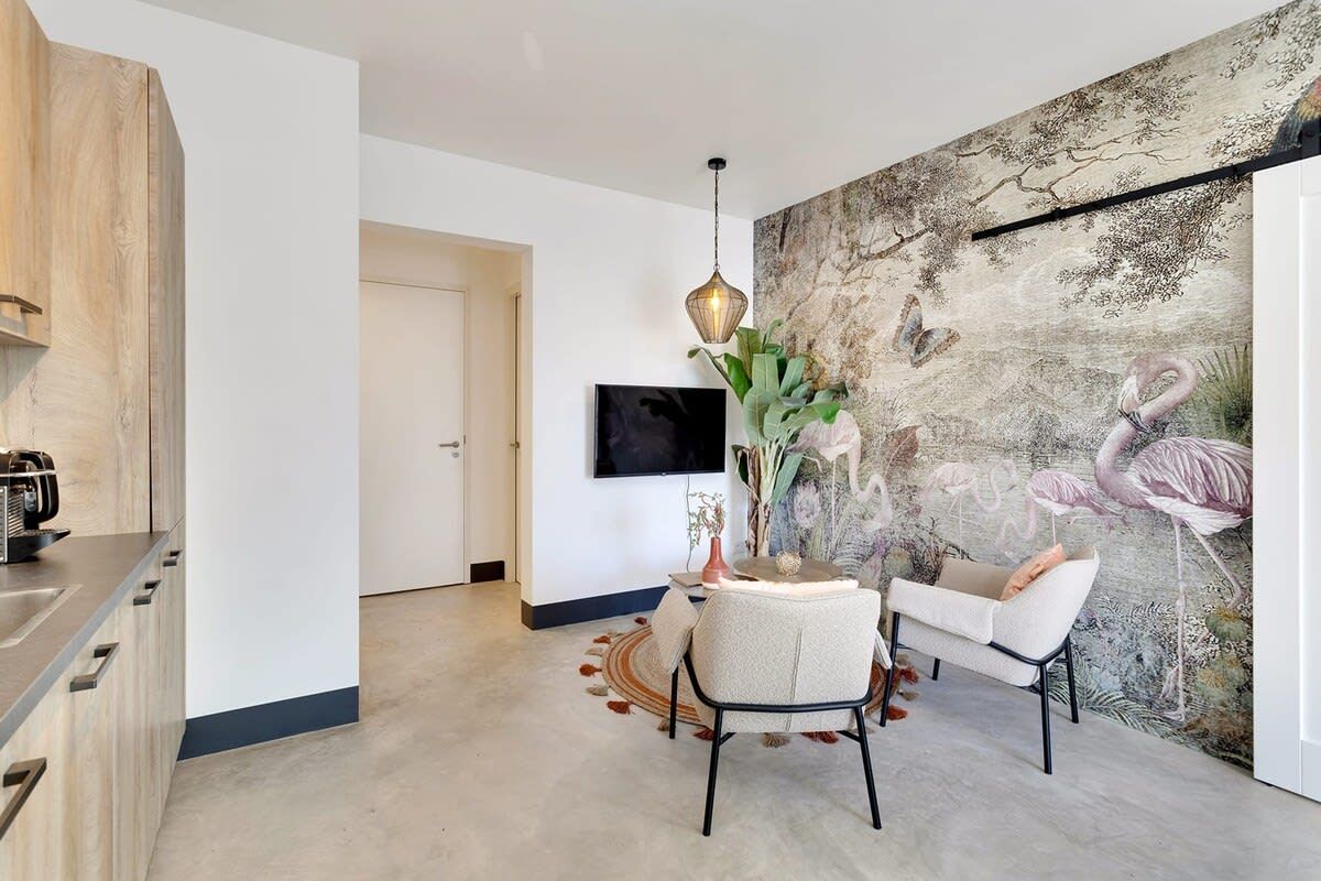 A modern living room with a flat-screen TV, a dining area with a round table and chairs, and a large wall mural.