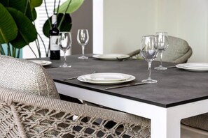 Une table à manger dressée avec des assiettes, des couverts et des verres à vin, avec une plante et une bouteille de vin en arrière-plan.