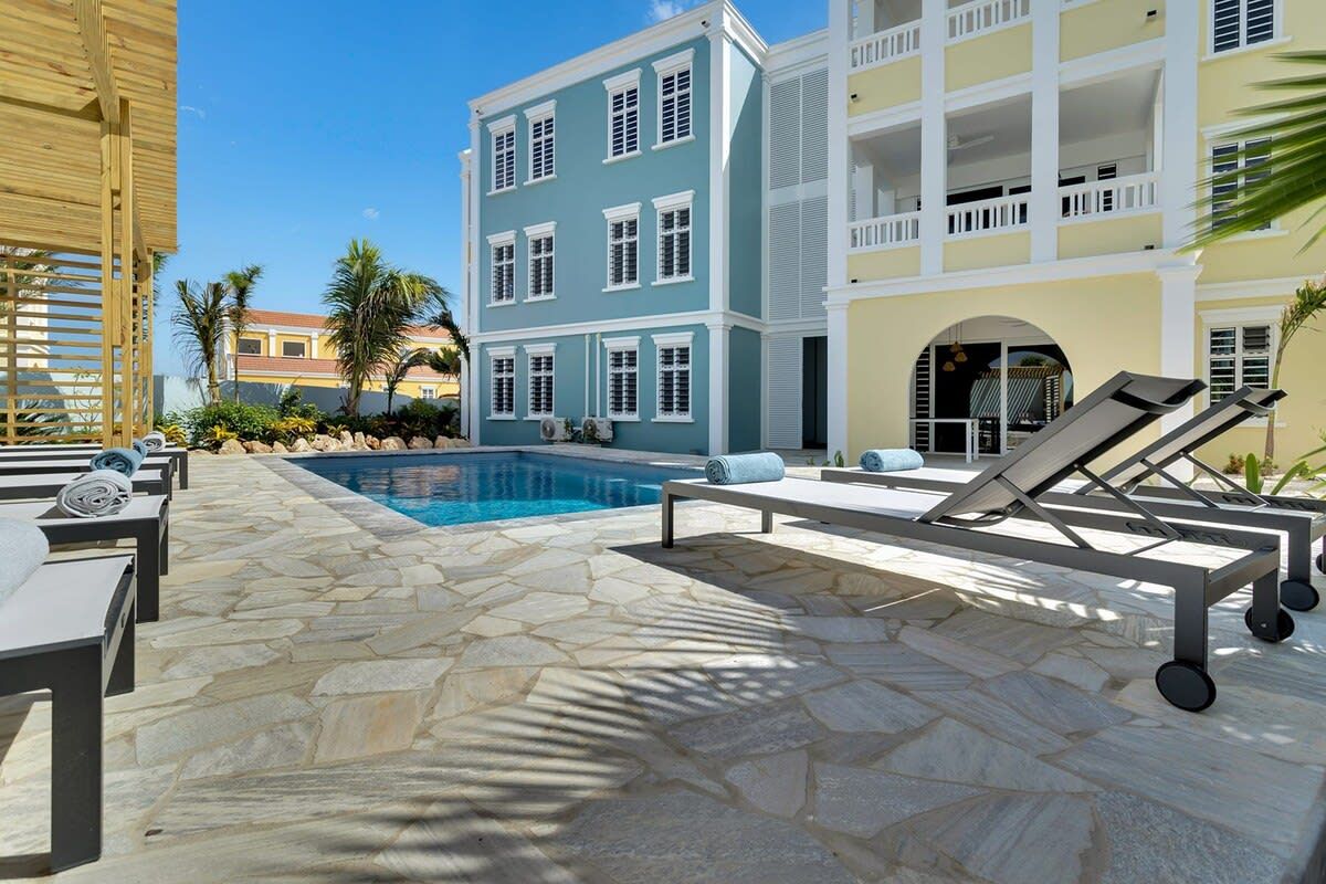 A poolside area with stone flooring, lounge chairs, and a pool.