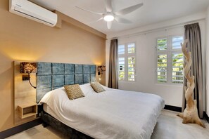 Une chambre à coucher comprenant un lit, un ventilateur de plafond, un appareil de climatisation, une fenêtre avec des rideaux et un tronc d’arbre décoratif.