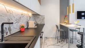 Una cocina moderna con salpicadero de mármol, encimera negra y un pequeño comedor con taburetes de bar.