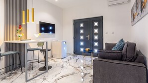 Una sala de estar moderna con suelo de mármol, un sofá gris con cojines, una mesita redonda y un televisor montado en la pared.