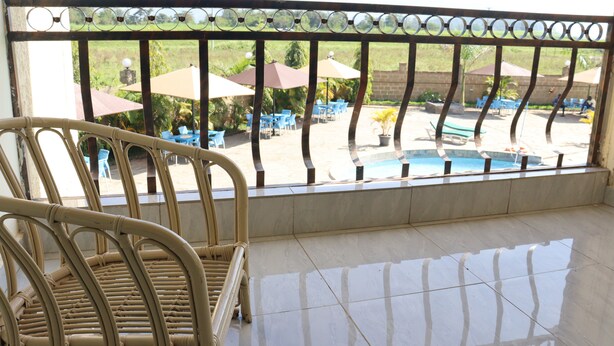 Un balcon avec un fauteuil en osier, un sol carrelé et une vue sur un espace piscine extérieur agrémenté de parasols et de chaises.