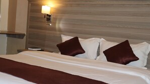 Un lit bien fait, avec une literie blanche et marron, une tête de lit en bois et un luminaire fixé au mur.