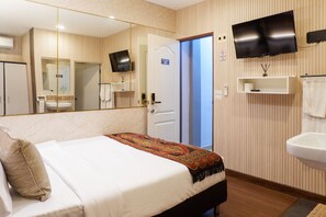 A hotel room with a bed, a large mirror, a television mounted on the wall, a sink, and a door leading to another room.