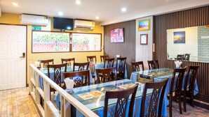 A restaurant with multiple tables and chairs, a TV mounted on the wall, and a window with a view of greenery. - Usman Halal Home (Bangkok)