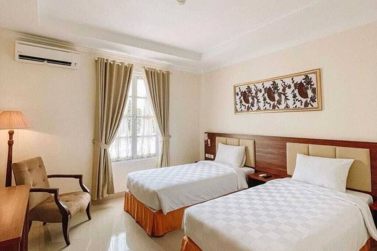 A hotel room with two beds, a desk, a chair, and a window with curtains.