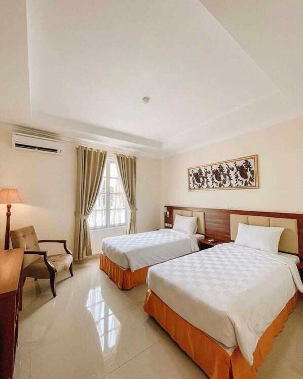 A hotel room with two beds, a desk, a chair, and a window with curtains. - LE SEMAR HOTEL KARAWACI (Tangerang)