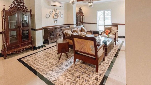Uma sala de estar espaçosa com teto alto, um armário de madeira grande, uma mesa de jantar com cadeiras e um tapete estampado.