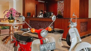 Uma área de recepção com um balcão de madeira, duas scooters antigas e uma planta decorativa.