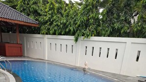 Uma piscina com borda azulejada, um pequeno elemento aquático e uma parede branca com janelas.